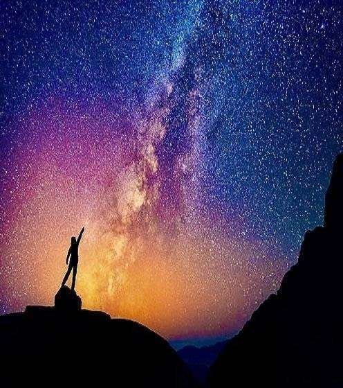 A person is standing next to the Milky Way galaxy pointing on a bright star.